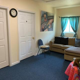 A cozy living room with a sofa, a clock on the wall, and a small window with curtains.