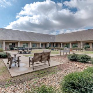A serene courtyard with benches and a well-maintained garden under a partly cloudy sky.