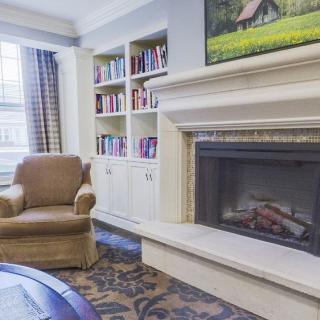 A cozy living room with a fireplace, armchair, and bookshelf.