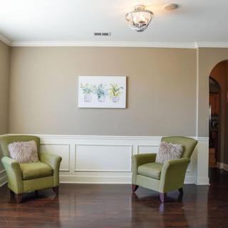 A minimalist living room with two green chairs, wall art, and a hardwood floor.
