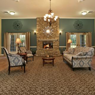 A traditionally decorated living room with a central stone fireplace, elegant furniture, and a grand chandelier.