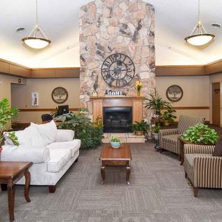 A cozy lounge area featuring a large fireplace, comfortable seating, and lush green plants.