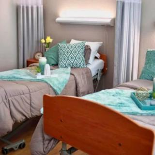 A neatly arranged hospital room with two beds, featuring teal accents and floral decorations.