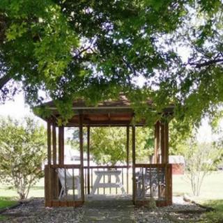 A wooden gazebo nestled in a lush garden surrounded by trees.