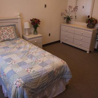A cozy bedroom with a single bed, dresser, and floral decorations.