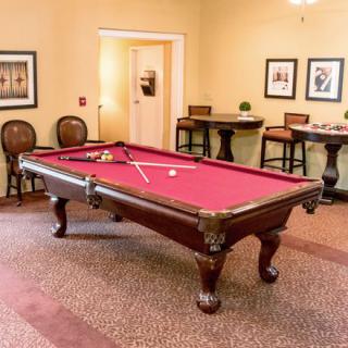 A cozy game room featuring a classic pool table with a red felt top, surrounded by elegant seating and wall art.