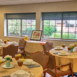 A beautifully set dining room ready for an event, featuring elegantly arranged tables and a view of the outdoors.