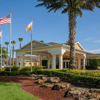 The entrance of a hotel surrounded by palm trees and flags under sunny skies.