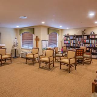 A cozy meeting room with arranged chairs, bookshelves, and a cross decoration.