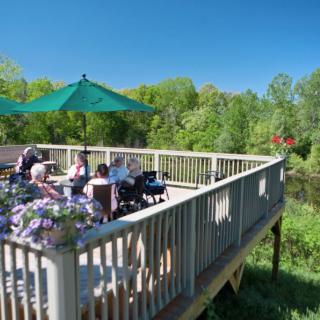 A group of people enjoying a sunny day on a raised deck with scenic views of lush greenery.