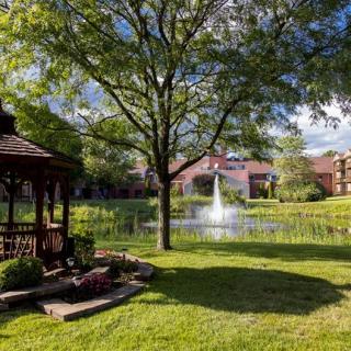 A peaceful park setting with a gazebo, large tree, and a pond with a fountain.