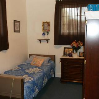 A simple bedroom with a single bed, brown curtains, and a dresser adorned with flowers and framed pictures.