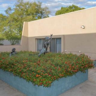 An outdoor sculpture in a garden setting, surrounded by greenery and adjacent to a modern building.