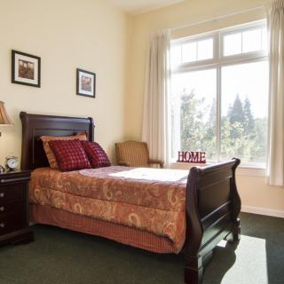 A cozy bedroom featuring a wooden bed with patterned bedding, a nightstand, and a large window flooding the room with natural light.