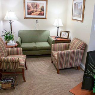 A cozy living room with a green sofa, striped armchairs, lamps, and wall art.