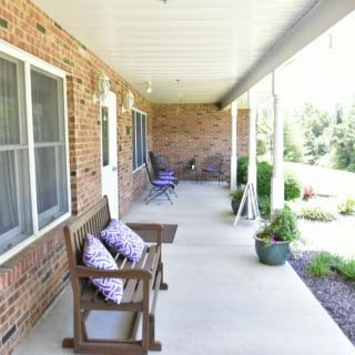 A cozy brick porch with seating and potted plants.