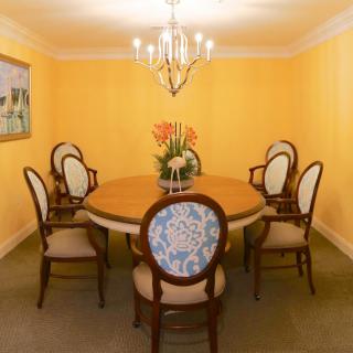 A dining room with a round table surrounded by six upholstered chairs, a chandelier overhead, and yellow walls.