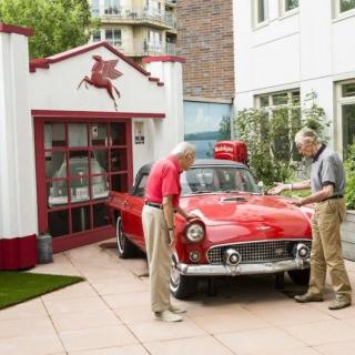 Two men examining a vintage red car in front of a garage with a Pegasus logo.
