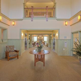 A spacious and elegantly decorated lobby with warm lighting, featuring a central wooden table and comfortable seating.