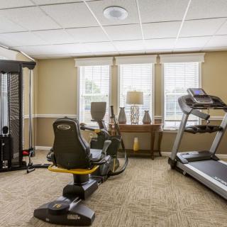 A well-lit fitness room with various exercise equipment, including a treadmill, stationary bike, and weight machine.