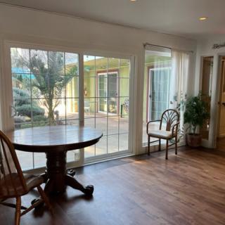 A bright dining area with large windows, featuring a round wooden table and chairs, complemented by a hardwood floor and natural light.