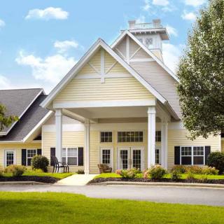 A picturesque view of a residential building with a prominent entrance, surrounded by greenery and under a partly cloudy sky.