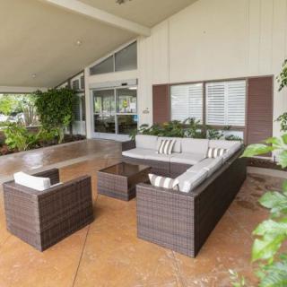 A modern outdoor patio with a comfortable seating arrangement, including a sofa set, armchair, and table surrounded by lush greenery.