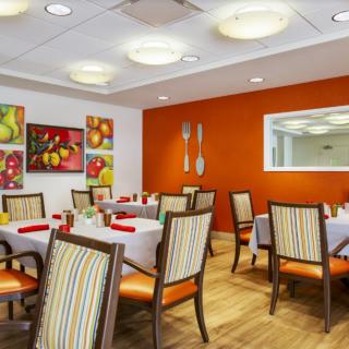 A modern dining room with vibrant orange walls, decorated with colorful artwork and equipped with neatly arranged tables and striped upholstered chairs.