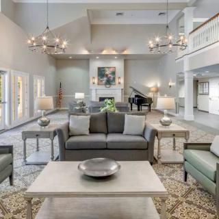 A spacious and elegantly designed living room featuring a central sofa, decorative coffee table, chandeliers, and a piano in the background.