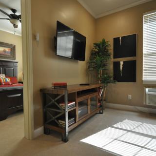 A cozy living room with a wall-mounted television and a wooden console, bathed in natural sunlight.