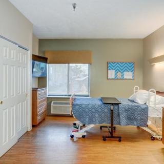 A hospital room featuring a bed, television, and window with outside view.