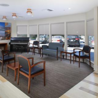 A spacious waiting room with several chairs, a piano, and large windows.