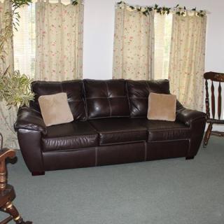 A cozy living room with a dark leather sofa adorned with two beige pillows, set against a backdrop of light-colored curtains.