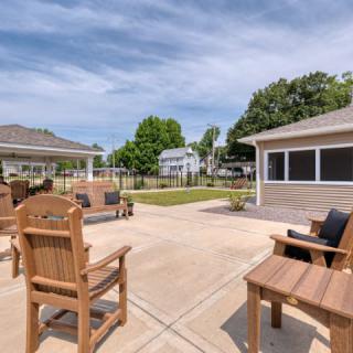 A spacious outdoor patio area with wooden furniture, surrounded by a garden on a sunny day.