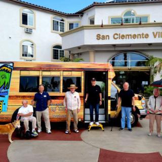 A group of people standing in front of a colorful bus near the San Clemente Villas entrance.
