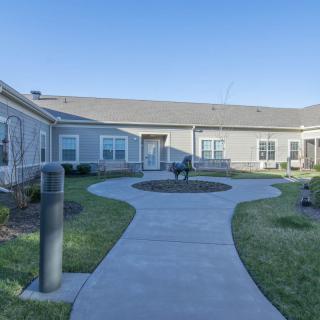 A serene courtyard with a pathway leading to a building, surrounded by well-maintained lawns and benches.