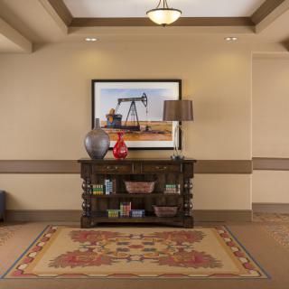 A decorated hallway with a table, vase, lamp, and painting above a patterned rug.