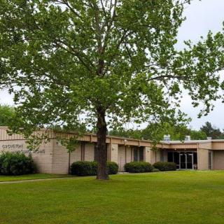 A view of a single-story building surrounded by a lush green lawn and trees.