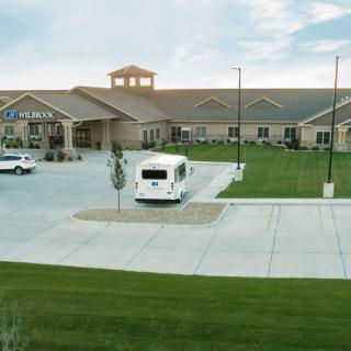 A building with a large parking lot and green lawn under a cloudy sky.