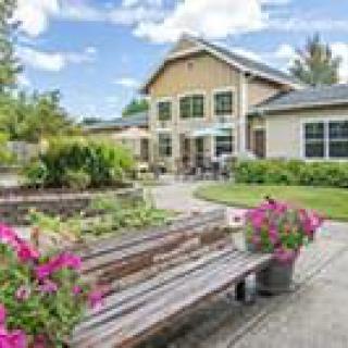 A picturesque garden setting with a wooden bench and colorful flowers in front of a charming house.