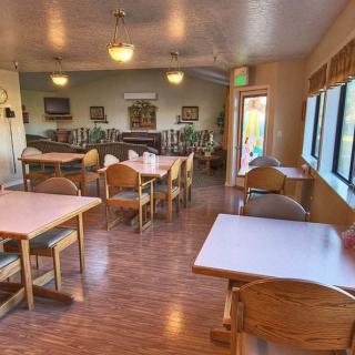 A cozy dining area with wooden tables and chairs, ambient lighting, and large windows providing natural light.