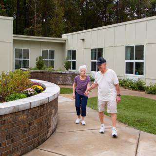 An elderly couple taking a walk outside their retirement home on a pleasant day.