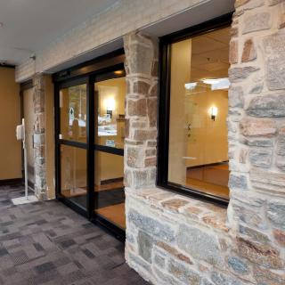 Modern building entrance with a stone facade and glass doors leading to a lobby.