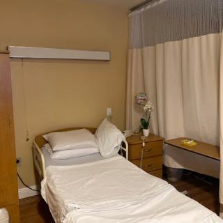 A clean and simple hospital room featuring a bed, bedside table, and curtains for privacy.