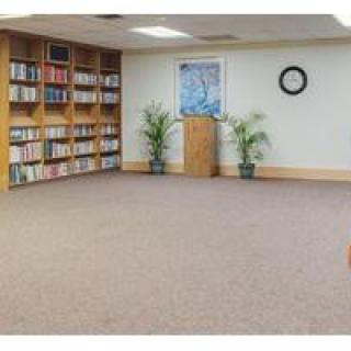 A quiet room with a bookshelf, podium, and plants, ideal for meetings or reading.