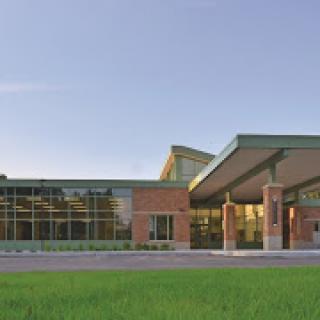 A modern educational or community building set against a clear sky and lush green grass.