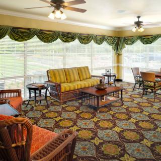 A cozy living room with patterned carpet, wicker furniture, and large windows.
