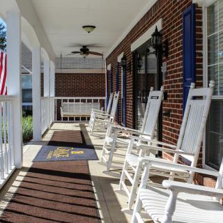 A welcoming porch with white rocking chairs and an American flag on a sunny day.