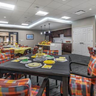 A modern dining area with decorated tables and vibrant chairs adjacent to a kitchen.