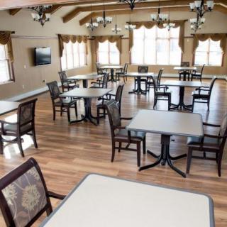 An empty dining room with neatly arranged tables and chairs, featuring large windows and elegant chandeliers.